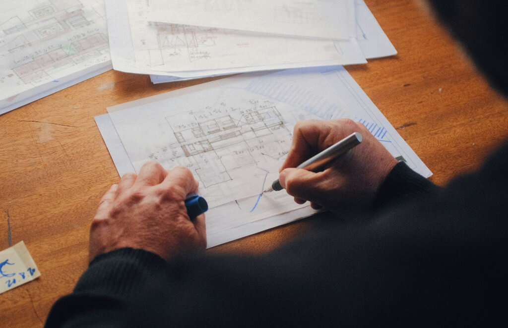 A person is focused on an electrical blueprint, using a pen to make detailed notes and adjustments.